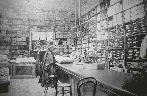 Antigua fotografía de un comercio de telas del siglo pasadado con estantes hasta el techo, donde dos clientes y los dos comerciantes miran a cámara